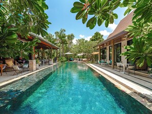 A clear blue pool with lounge chairs and umbrellas, surrounded by lush greenery and a covered seating area. - Coco Retreat Phuket Resort & Spa (Chalong)