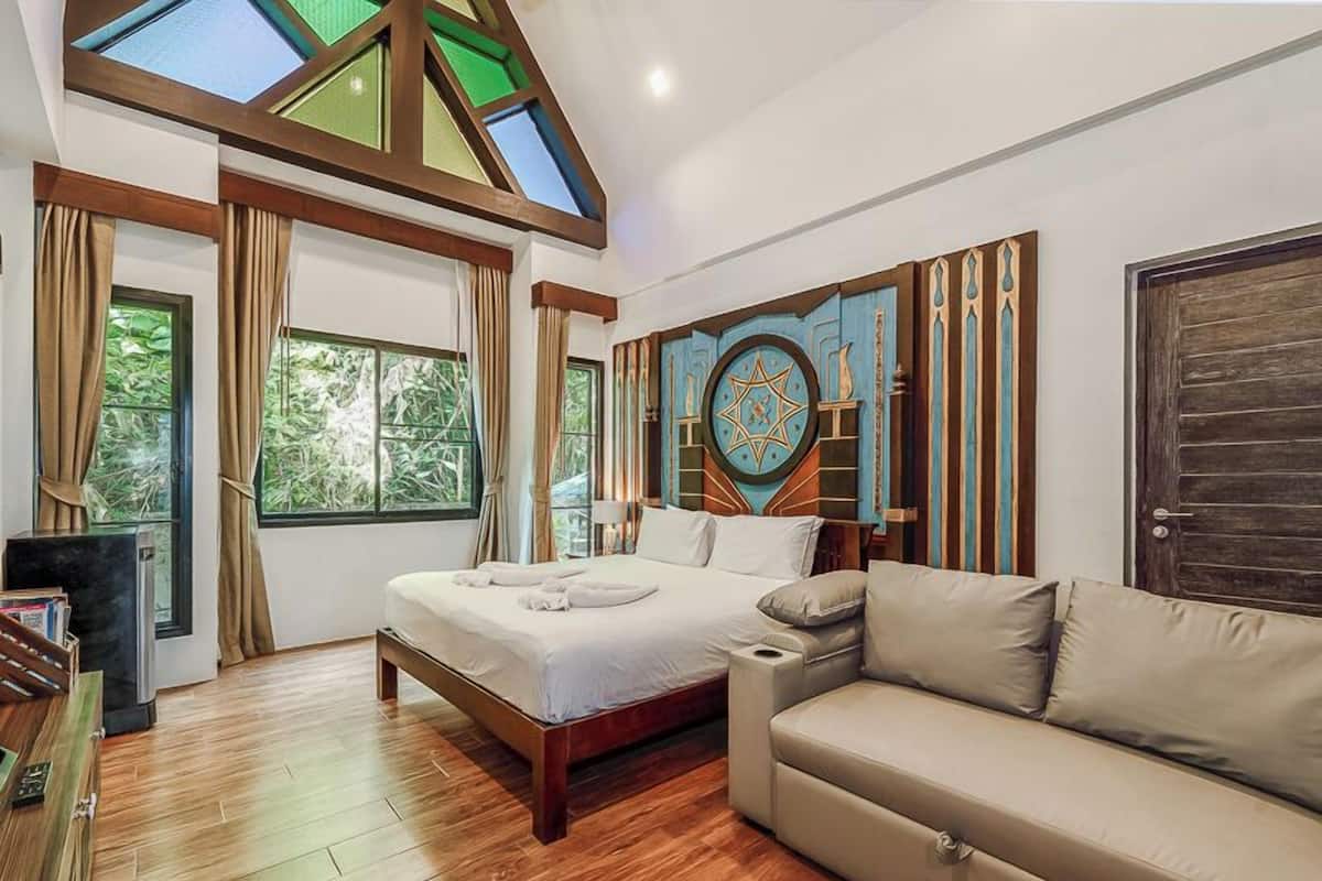 A bedroom with a bed, a sofa, a large window, and a decorative wall piece.