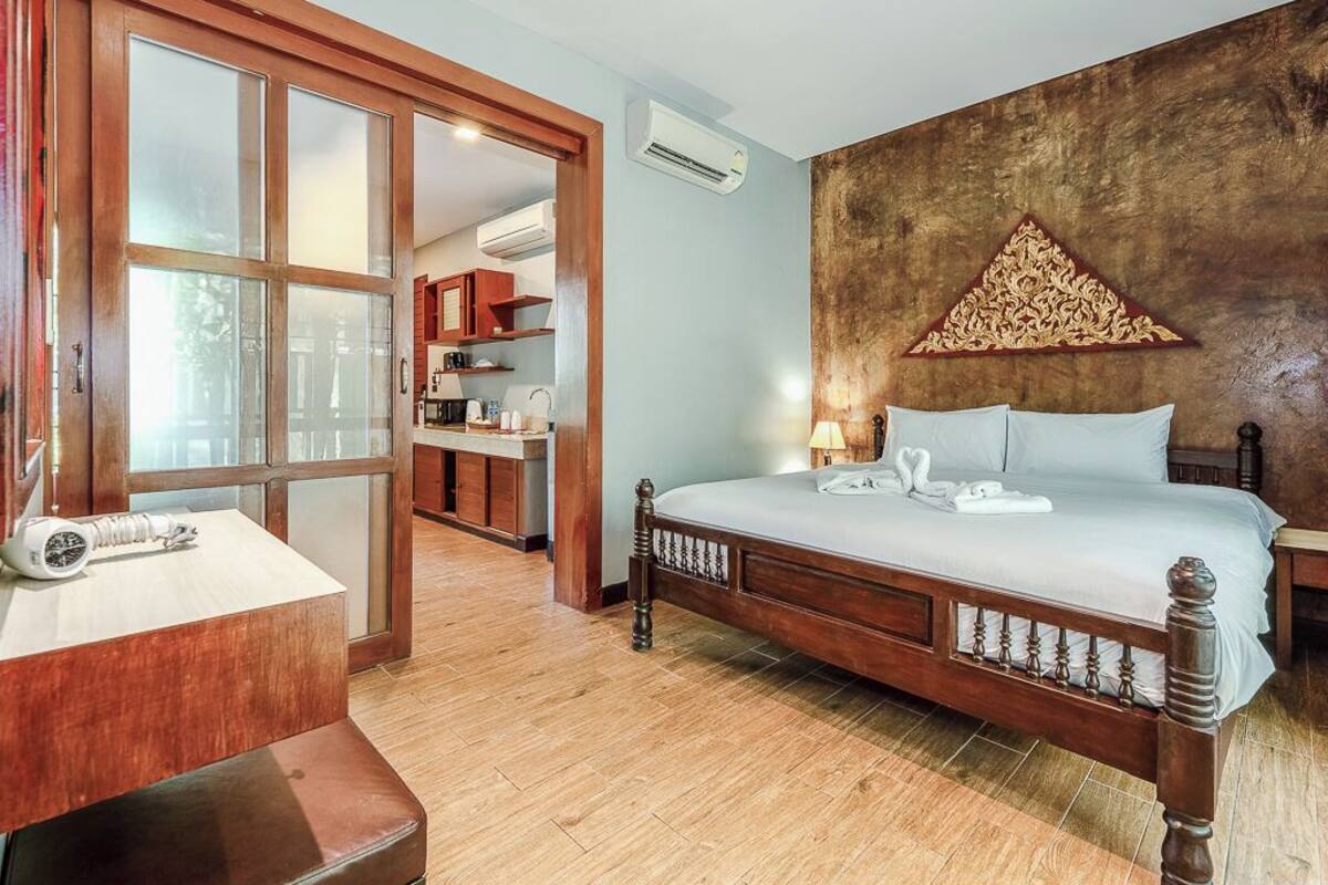 A bedroom with a wooden bed, a nightstand, a desk with a lamp, and a large window.