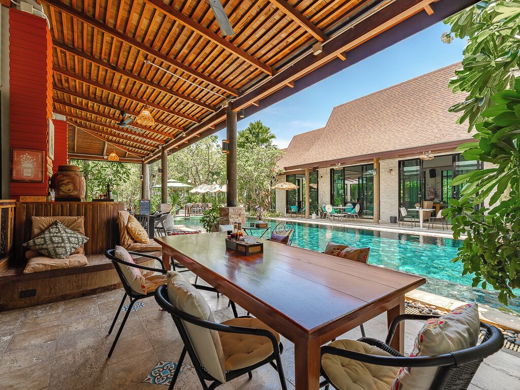 Ein Sitzbereich im Freien mit Blick auf einen Pool, Holzmöbel und eine überdachte Terrasse.