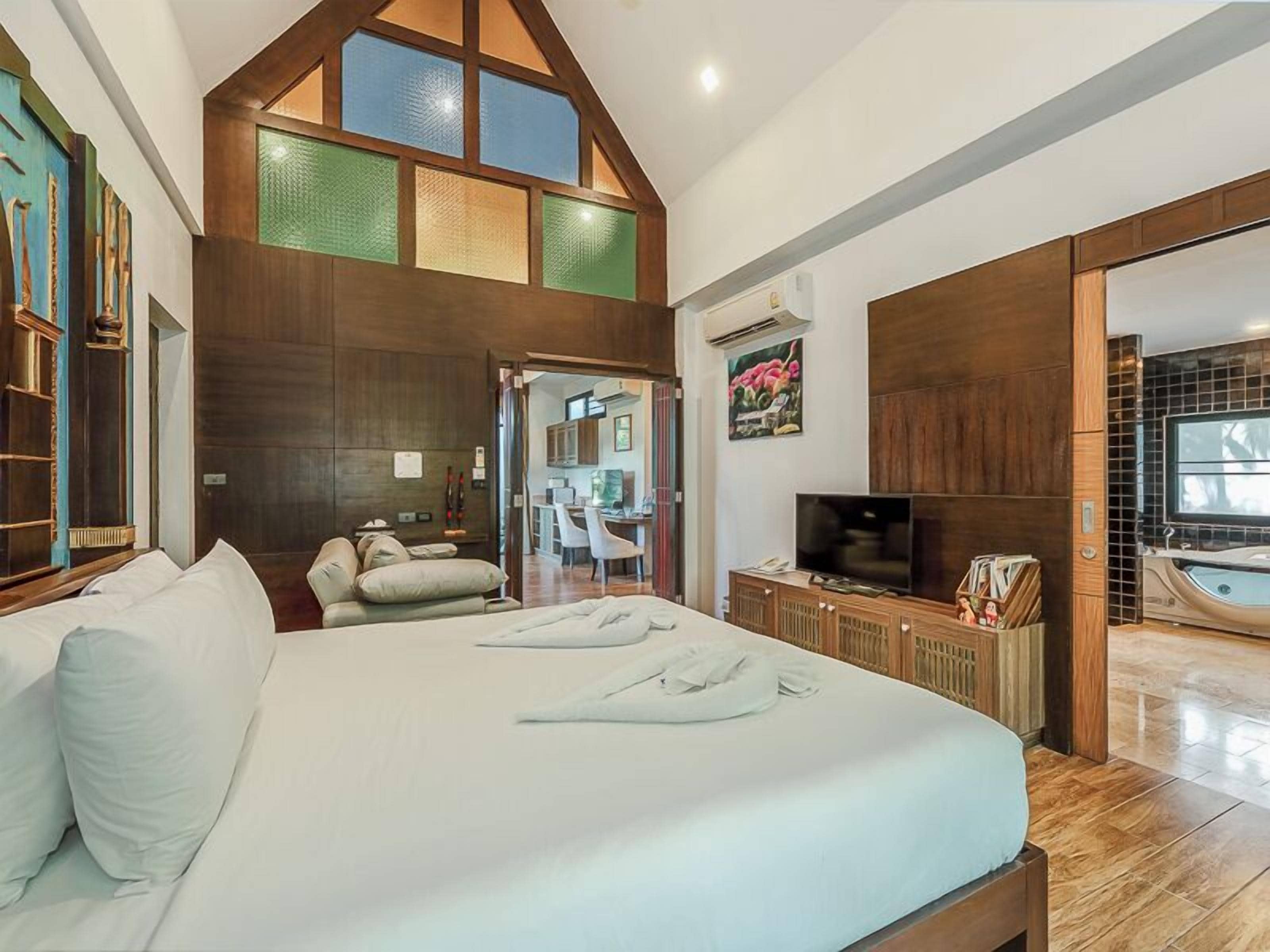 A bedroom with a large bed, a television, a bathroom with a bathtub, and a kitchen area.