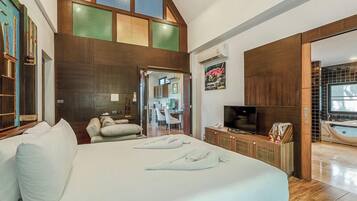 A bedroom with a large bed, a television, a bathroom with a bathtub, and a kitchen area.