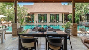 Ein Außenpoolbereich mit überdachter Lounge, einem Esstisch und Stühlen.