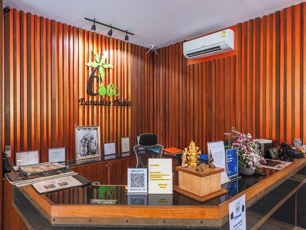 Un comptoir d'accueil avec un mur composé de lattes de bois, un logo, un certificat encadré, un ordinateur, un téléphone et une petite statue.