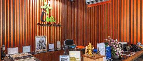 Un comptoir d'accueil avec un mur composé de lattes de bois, un logo, un certificat encadré, un ordinateur, un téléphone et une petite statue.