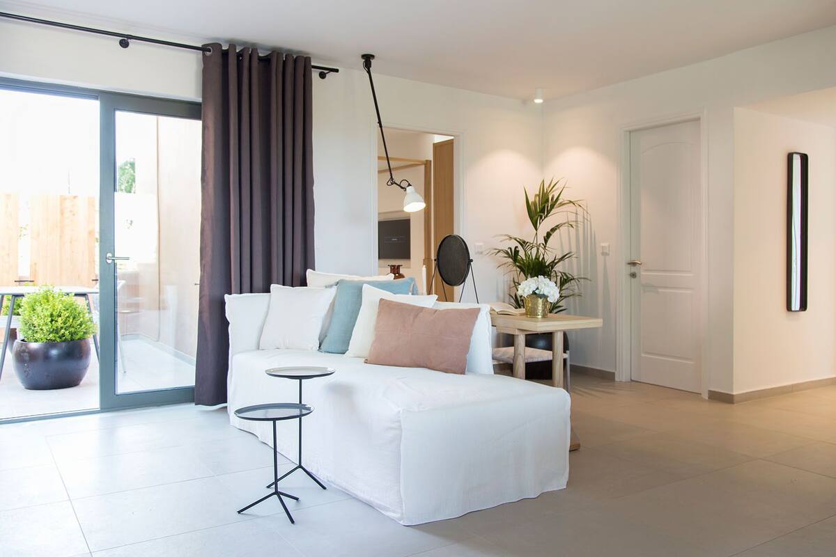 Une chambre moderne avec un lit blanc, une petite table ronde et une plante en pot.