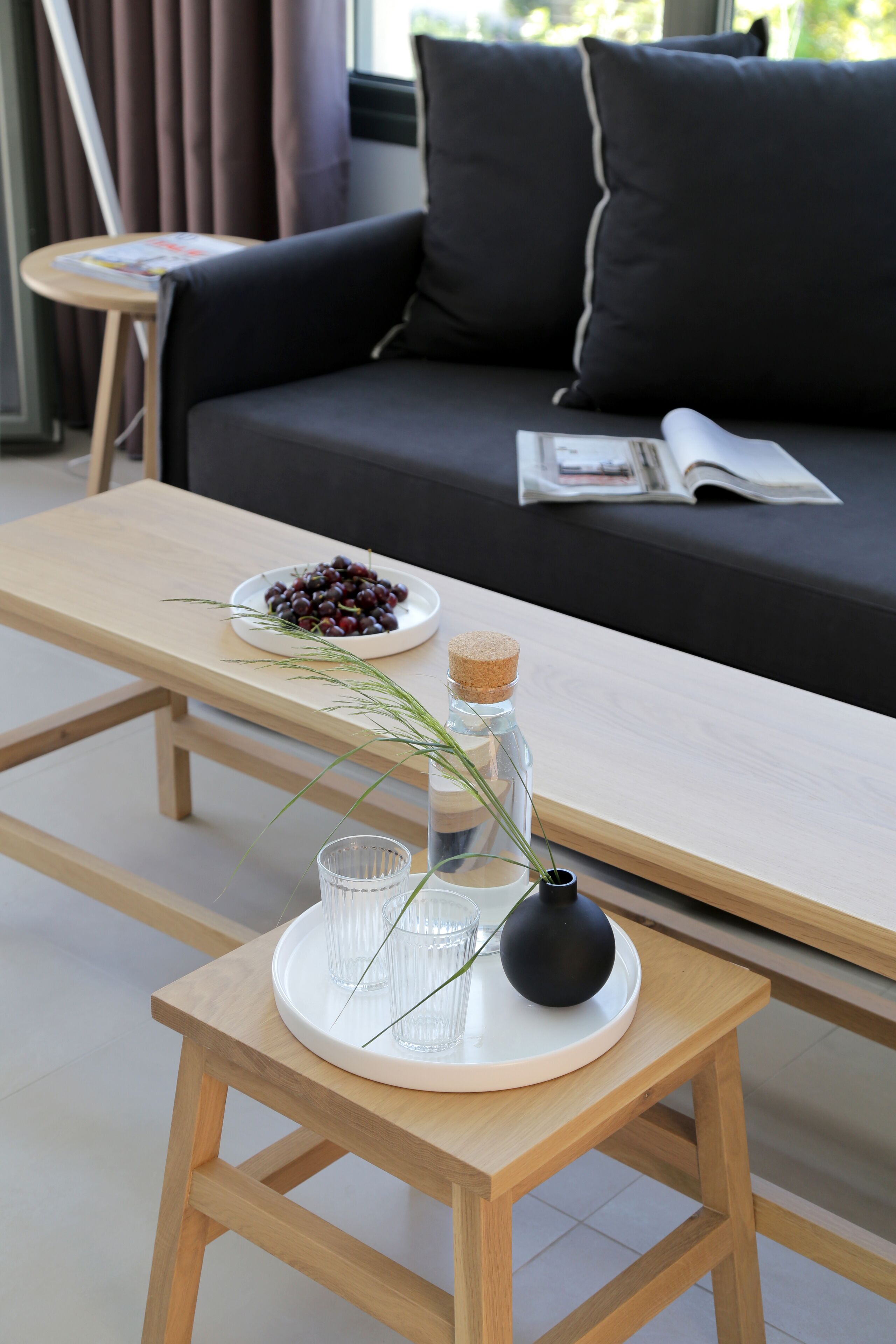 A modern living room with a wooden coffee table, a black sofa, and a small side table with a magazine.