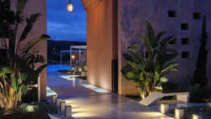 Una entrada de hotel moderna con piscina, columnas imponentes y plantas tropicales.