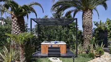 Un jacuzzi bajo una pérgola de madera rodeado de palmeras y abundante vegetación.