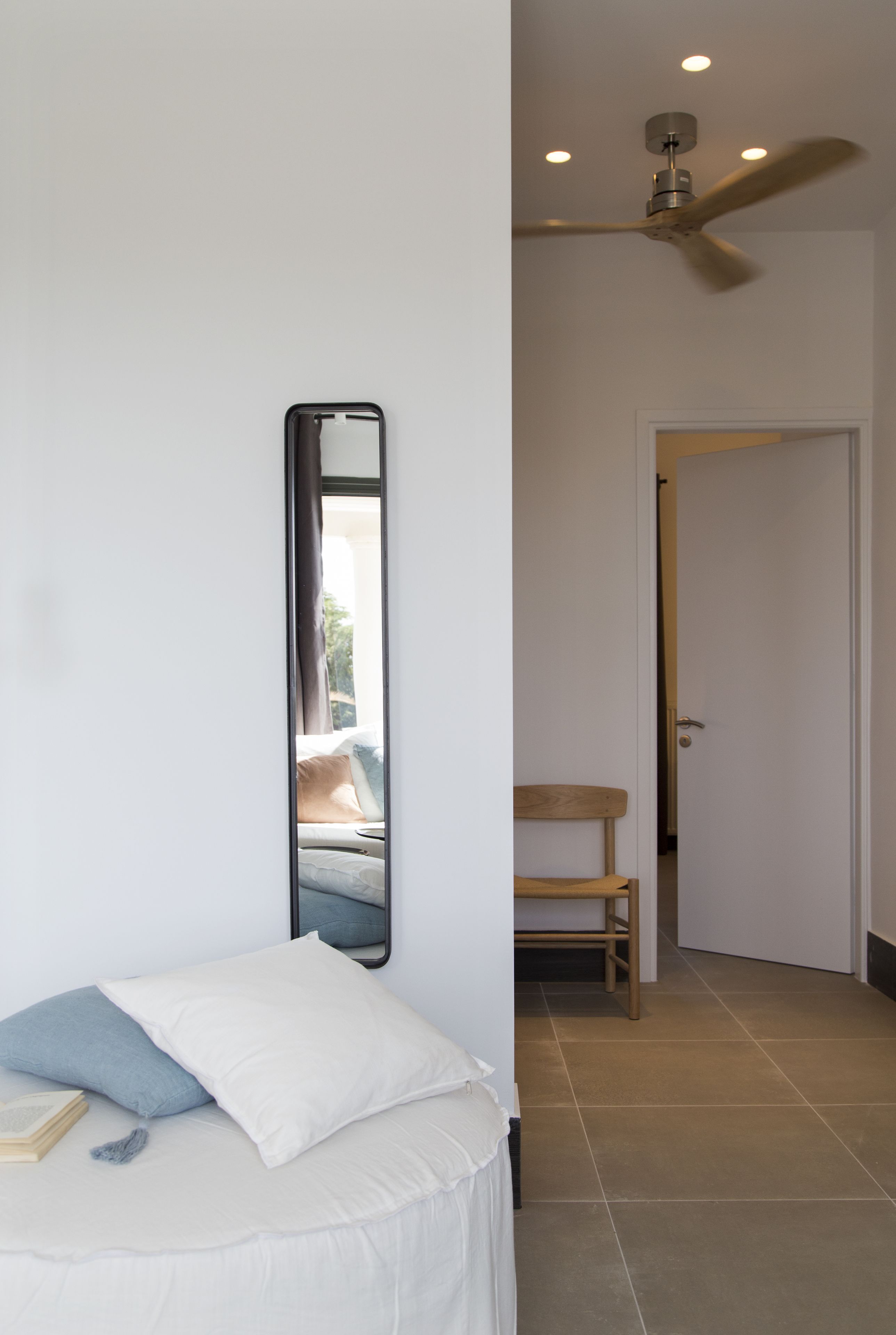 Un dormitorio con cama, un espejo grande, un ventilador de techo y una puerta que da a otra habitación.