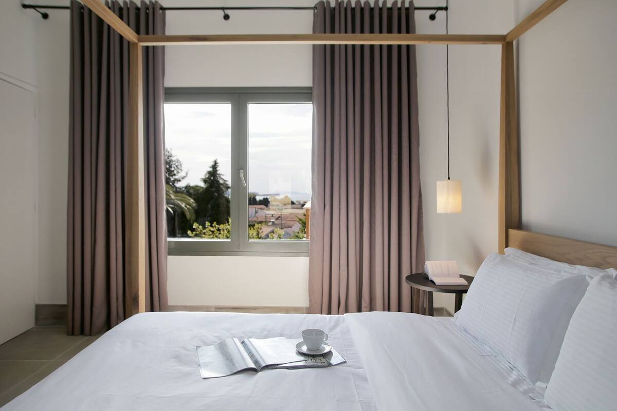 Une chambre d’hôtel moderne avec un grand lit, une petite table de chevet avec une lampe et une fenêtre avec des rideaux.