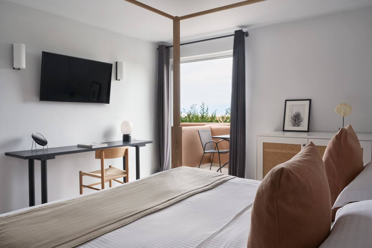 Une chambre d’hôtel moderne dotée d’un grand lit, d’un bureau avec une chaise, d’une télévision à écran plat et d’un balcon avec vue.