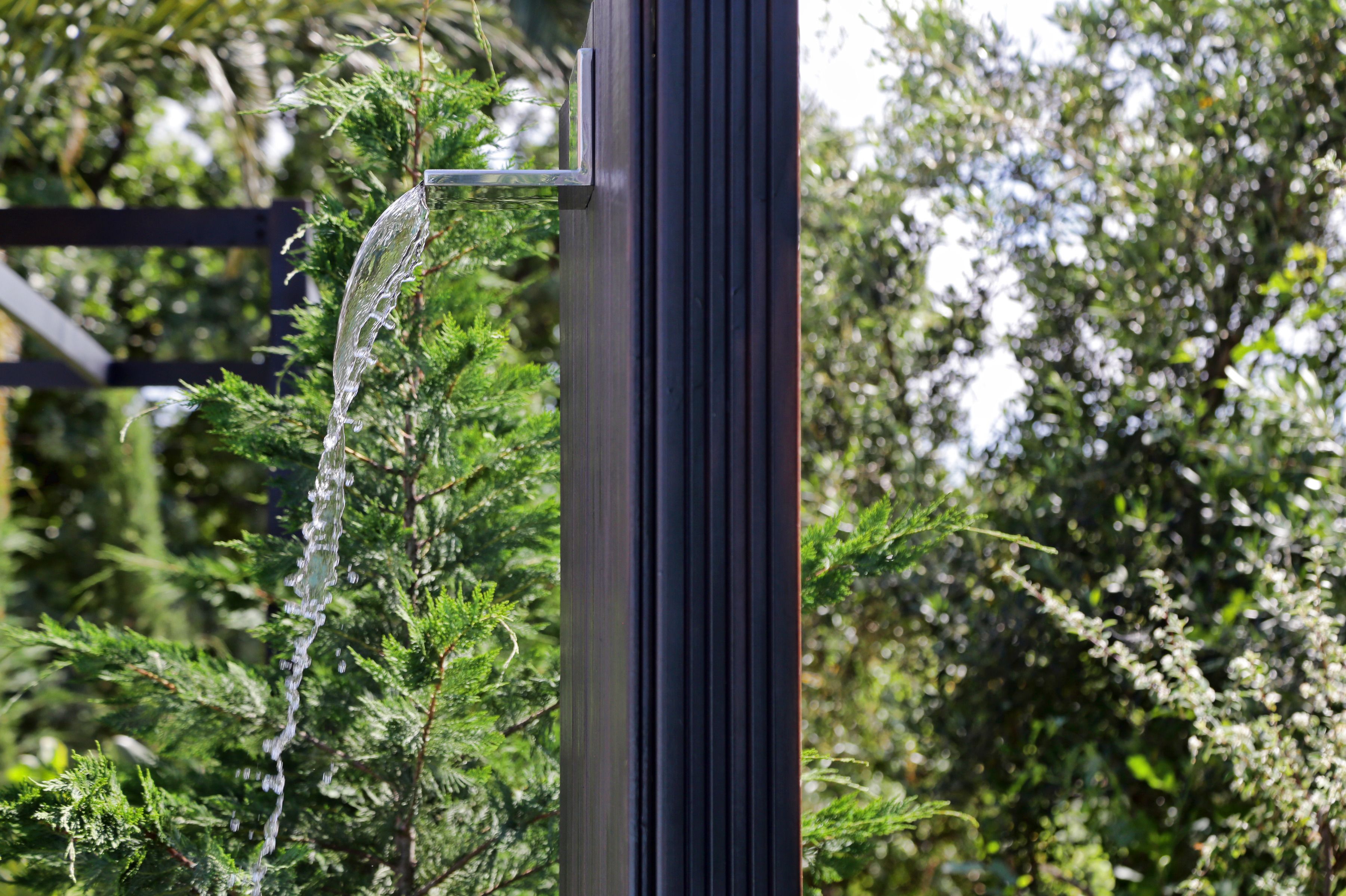 A water feature with a clear stream flowing over a metal structure, surrounded by lush greenery.
