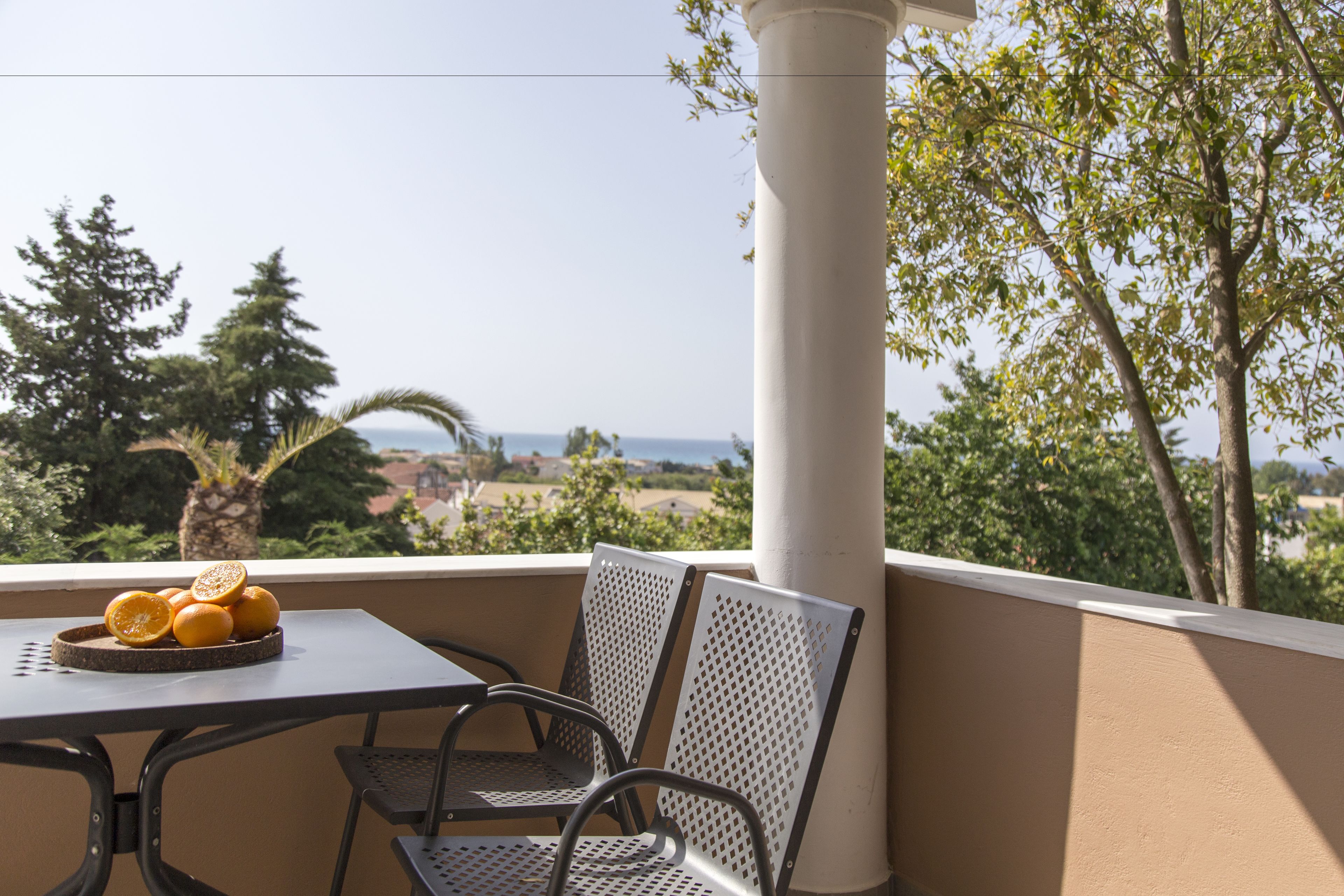 Ein Balkon mit Tisch und Stühlen, eine Schale Orangen und Blick auf das Meer und Bäume.