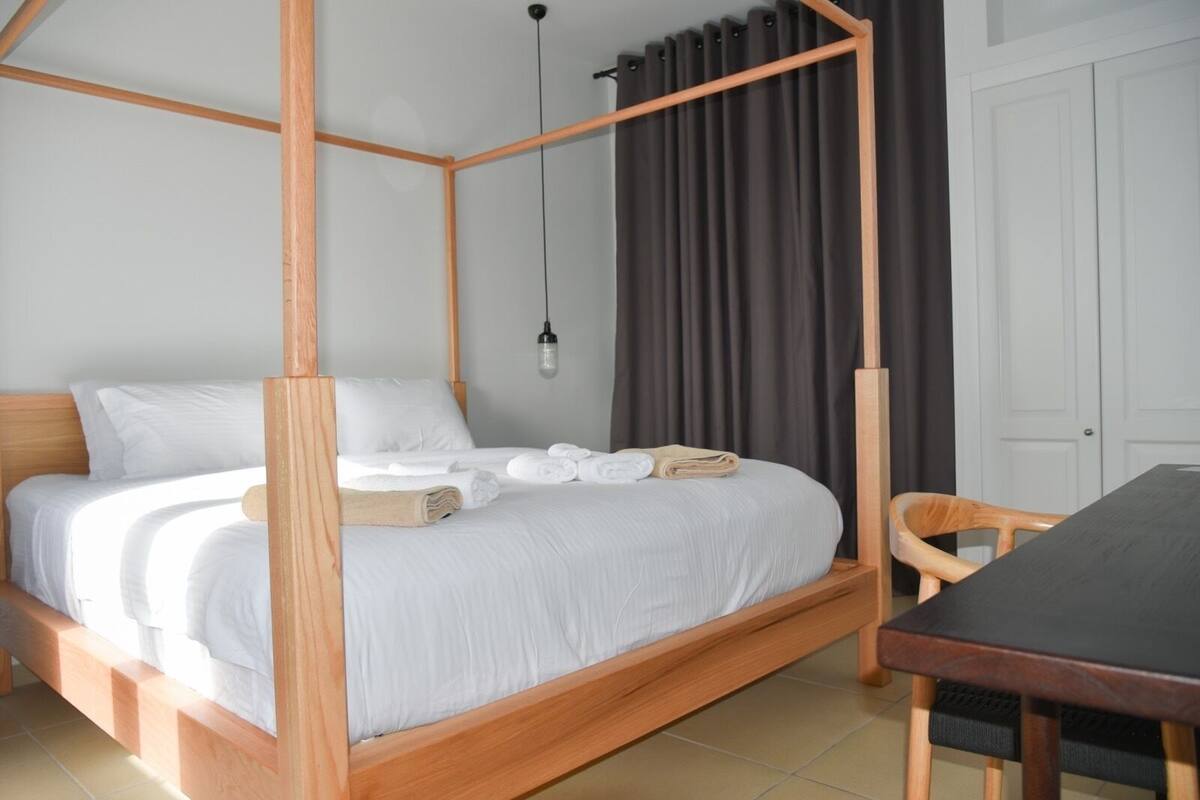 Un lit à baldaquin avec du linge de lit blanc, une tête de lit en bois et une table recouverte d’une nappe noire.