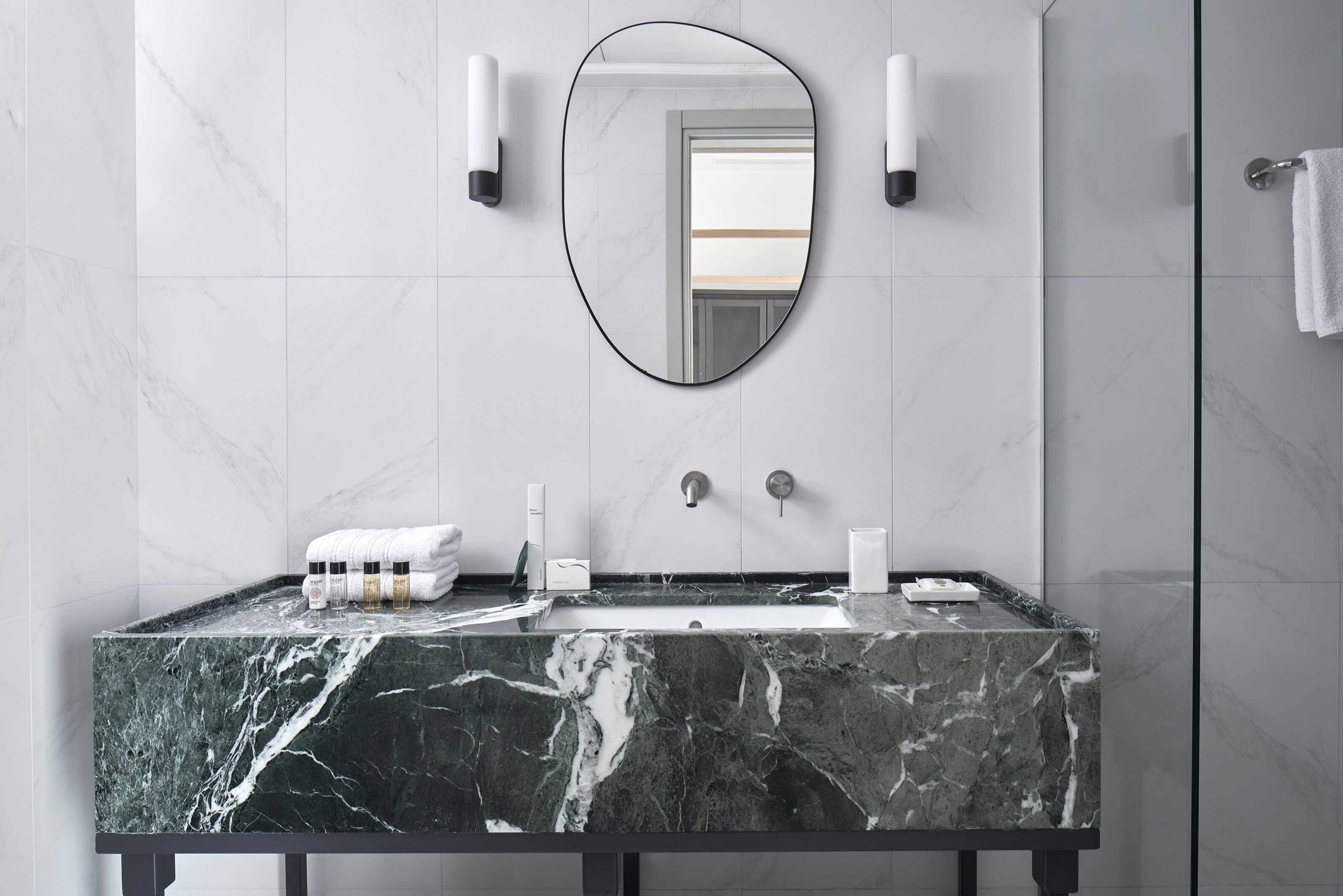 A modern bathroom with a marble sink, a large mirror, and two wall-mounted lights.