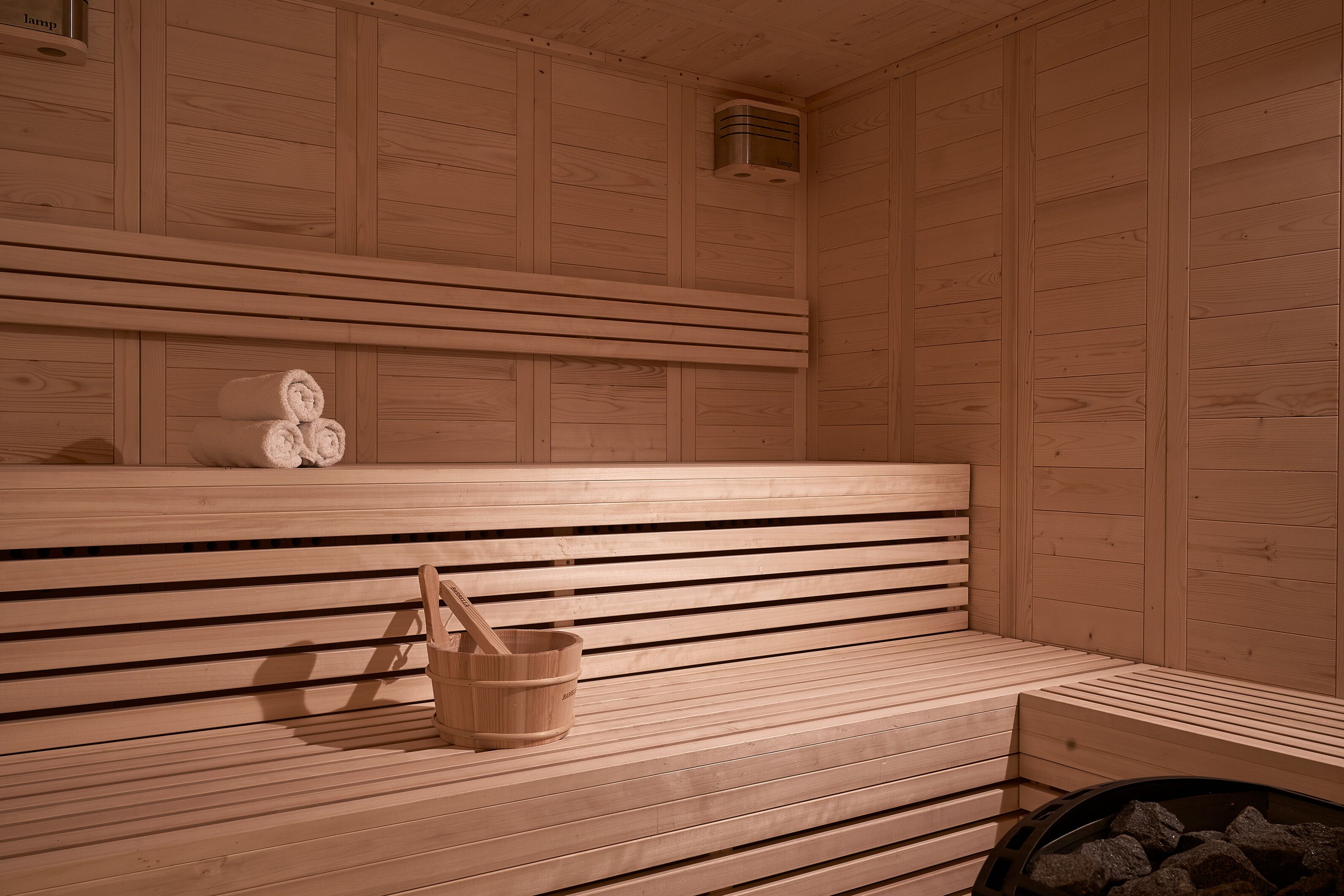 Eine Holzsauna mit Bänken, einem Eimer und einem Ofen.