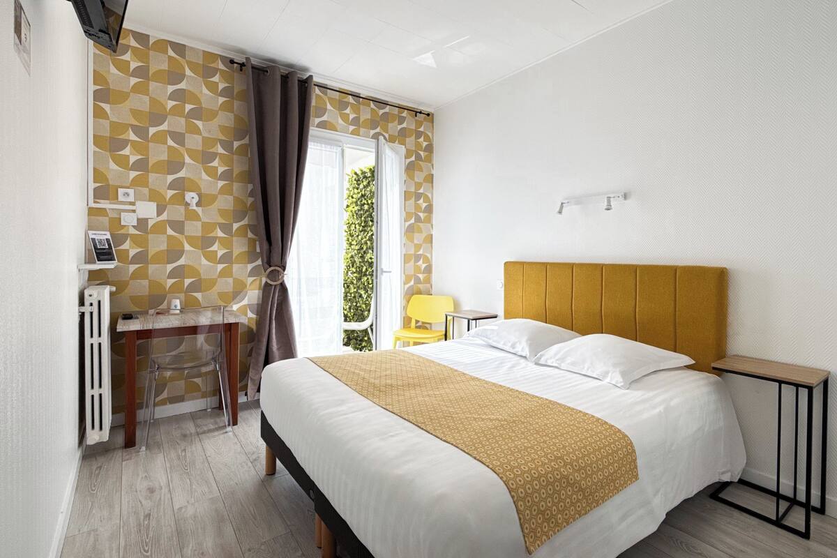 A hotel room with a bed, a desk, a chair, and a window with curtains.