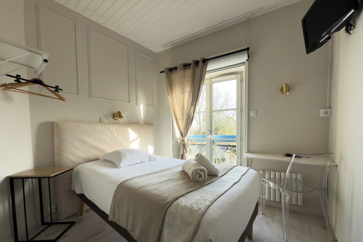A bedroom with a bed, a bedside table, a window with curtains, a TV mounted on the wall, and a radiator.