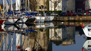 Ein Hafen mit vertäuten Booten, ein historischer Turm und ein Gebäude mit einer Kuppel.