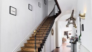 Eine Treppe mit Holzboden und schwarzen Geländern, die zu einem Zwischenpodest mit einer weißen Wand und gerahmten Kunstwerken führt.