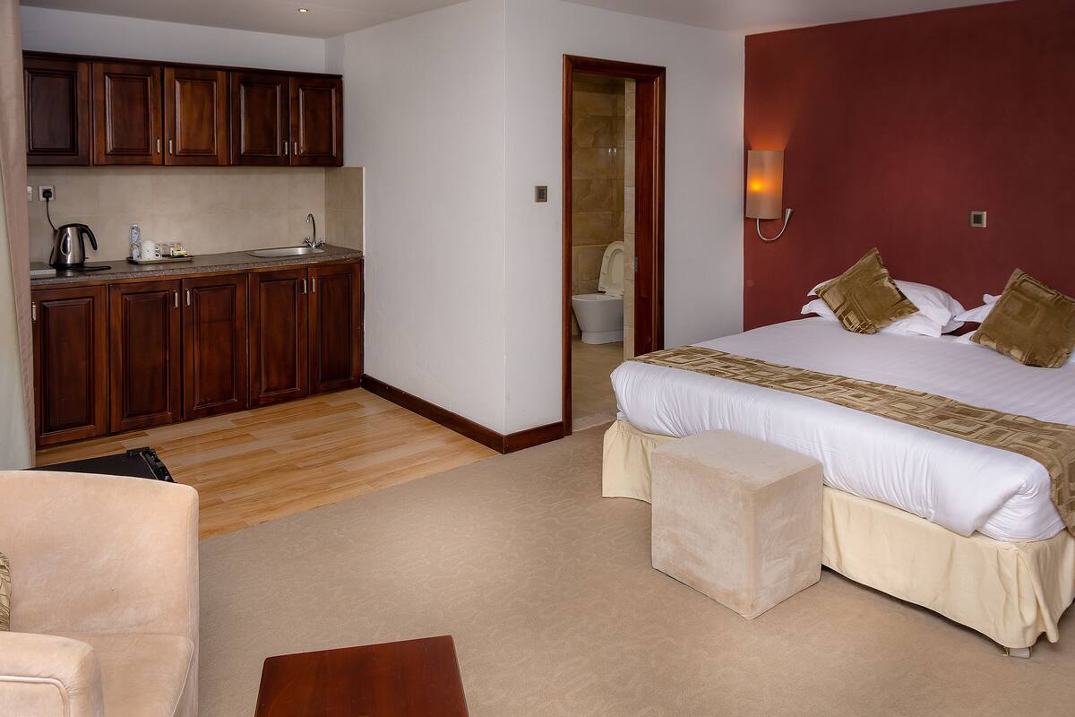 A hotel room with a bed, a small sofa, a wooden cabinet, a kitchenette, and a bathroom.