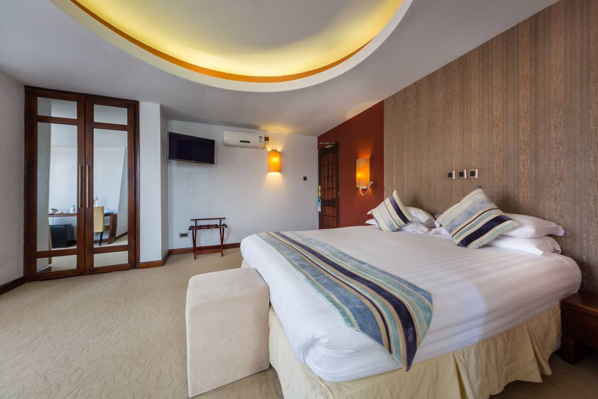 A modern hotel room with a large bed, a TV, and a wooden wardrobe.