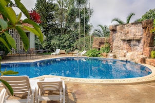 Una piscina con sillas de descanso, rodeada de follaje y un muro de piedra.