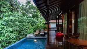 Una terraza de madera con piscina, rodeada de abundante vegetación.