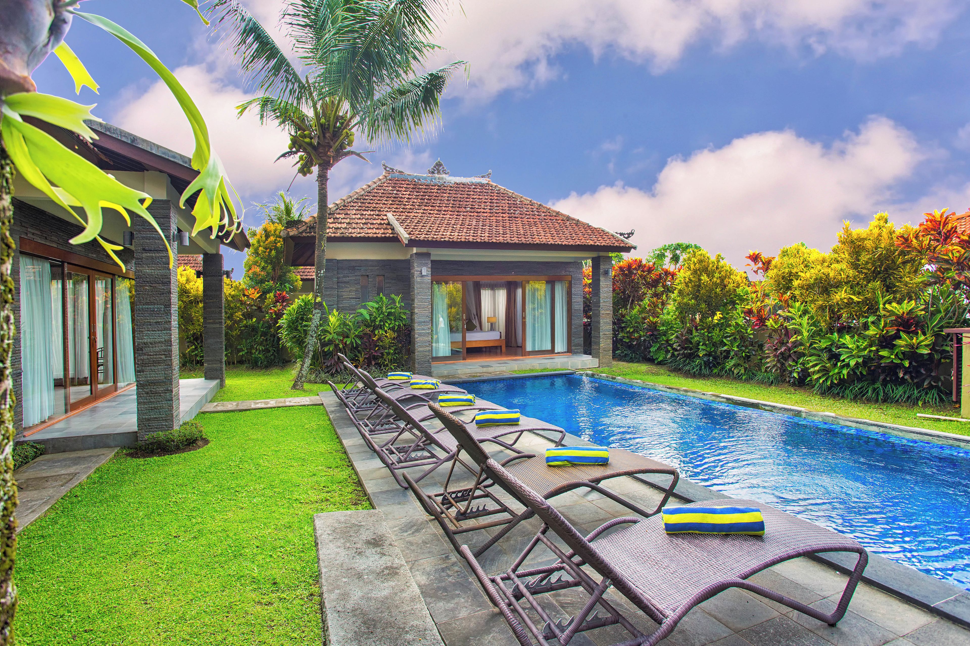Un espace aménagé au bord de la piscine, avec des chaises longues et une vue dégagée sur une maison dont le toit est recouvert de tuiles.