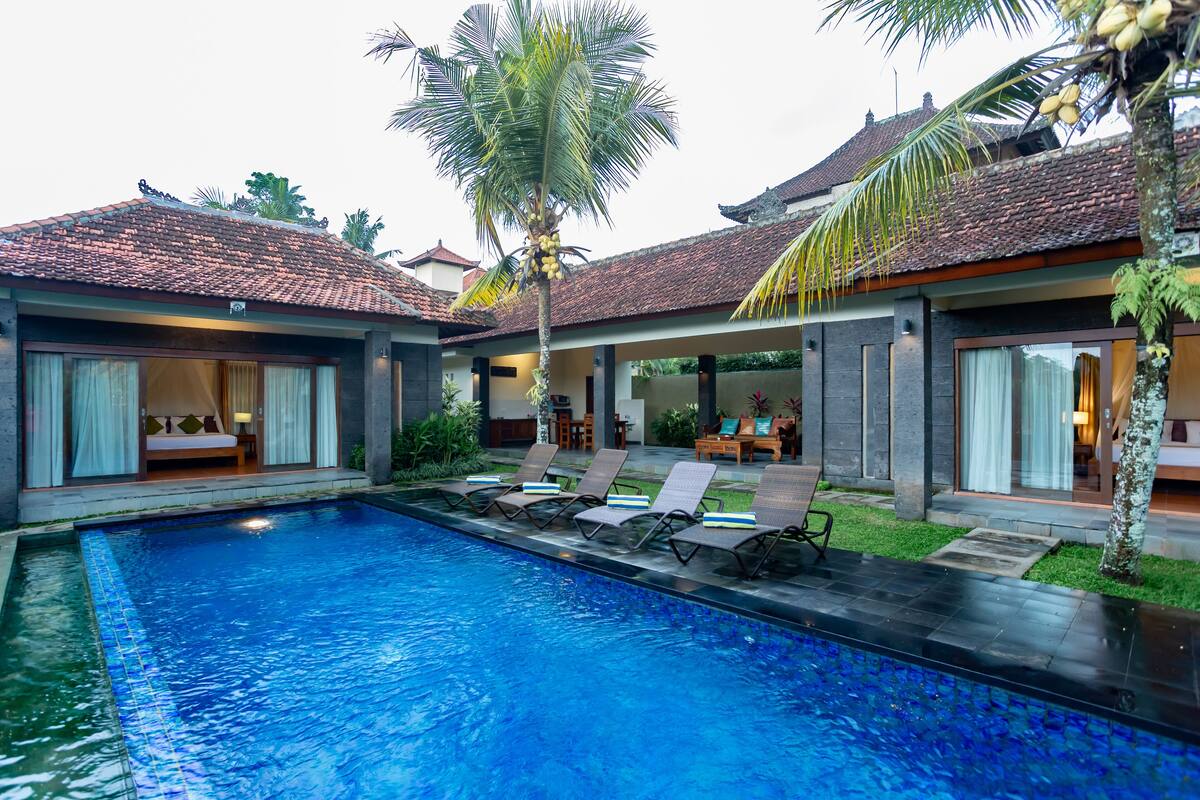A swimming pool with lounge chairs, a covered seating area, and a traditional tiled roof.