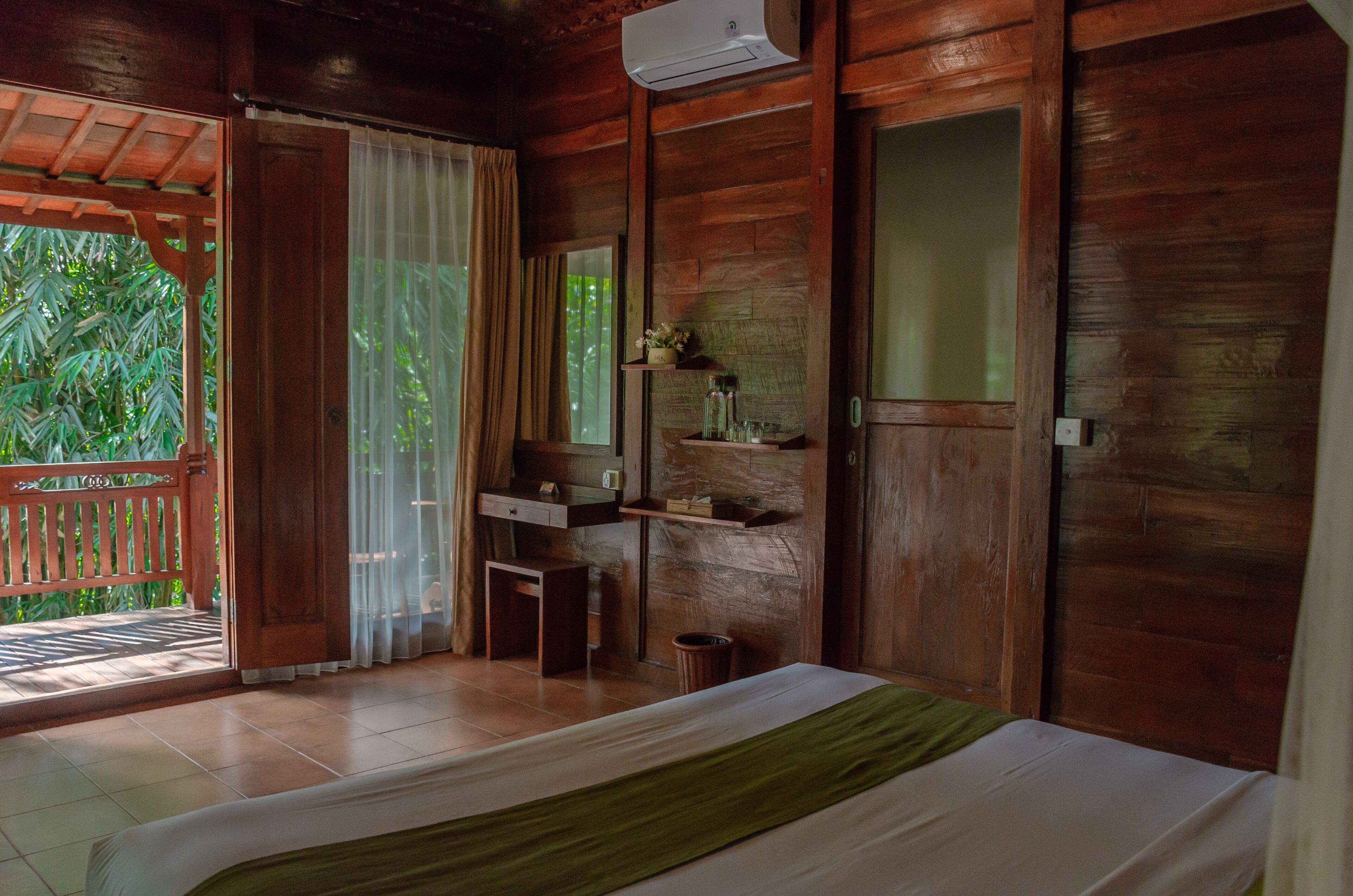 A wooden room with a bed, a small desk, a mirror, and shelves with decorative items.