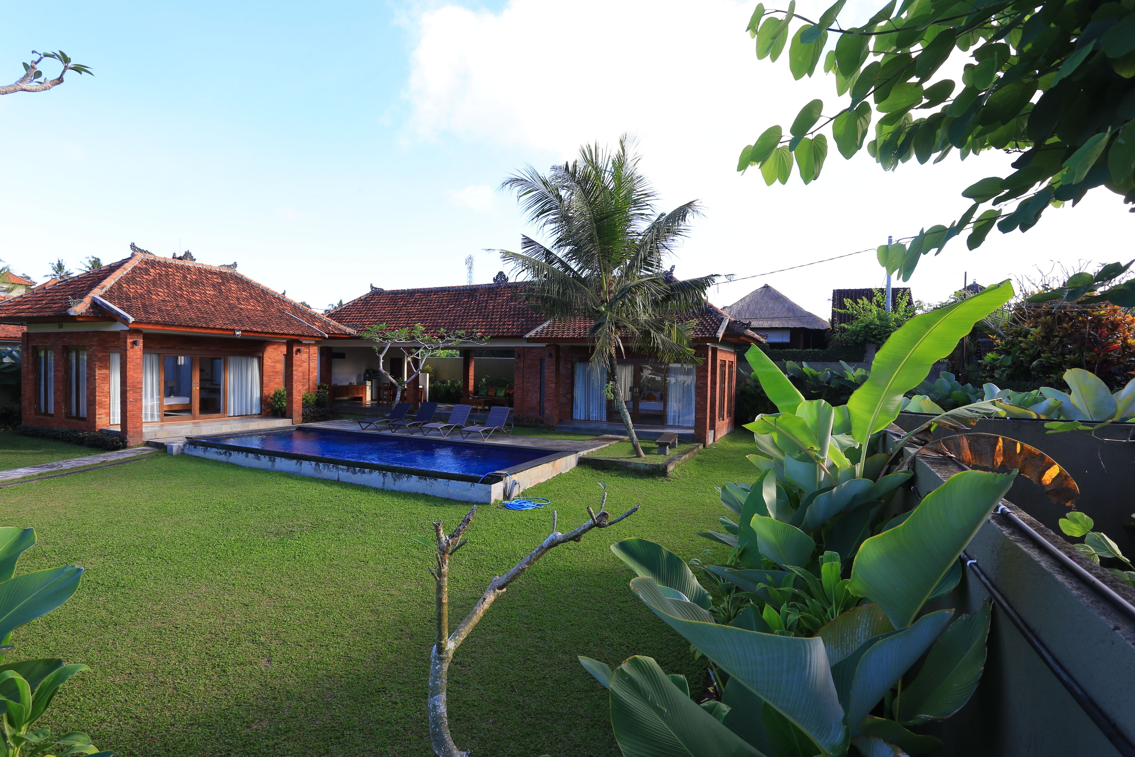 A residential property with a swimming pool, a well-maintained lawn, and a brick house with a tiled roof.