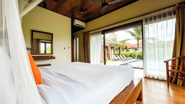 A hotel room with a bed, a wooden bench, a large window with curtains, and a view of a pool and greenery outside.