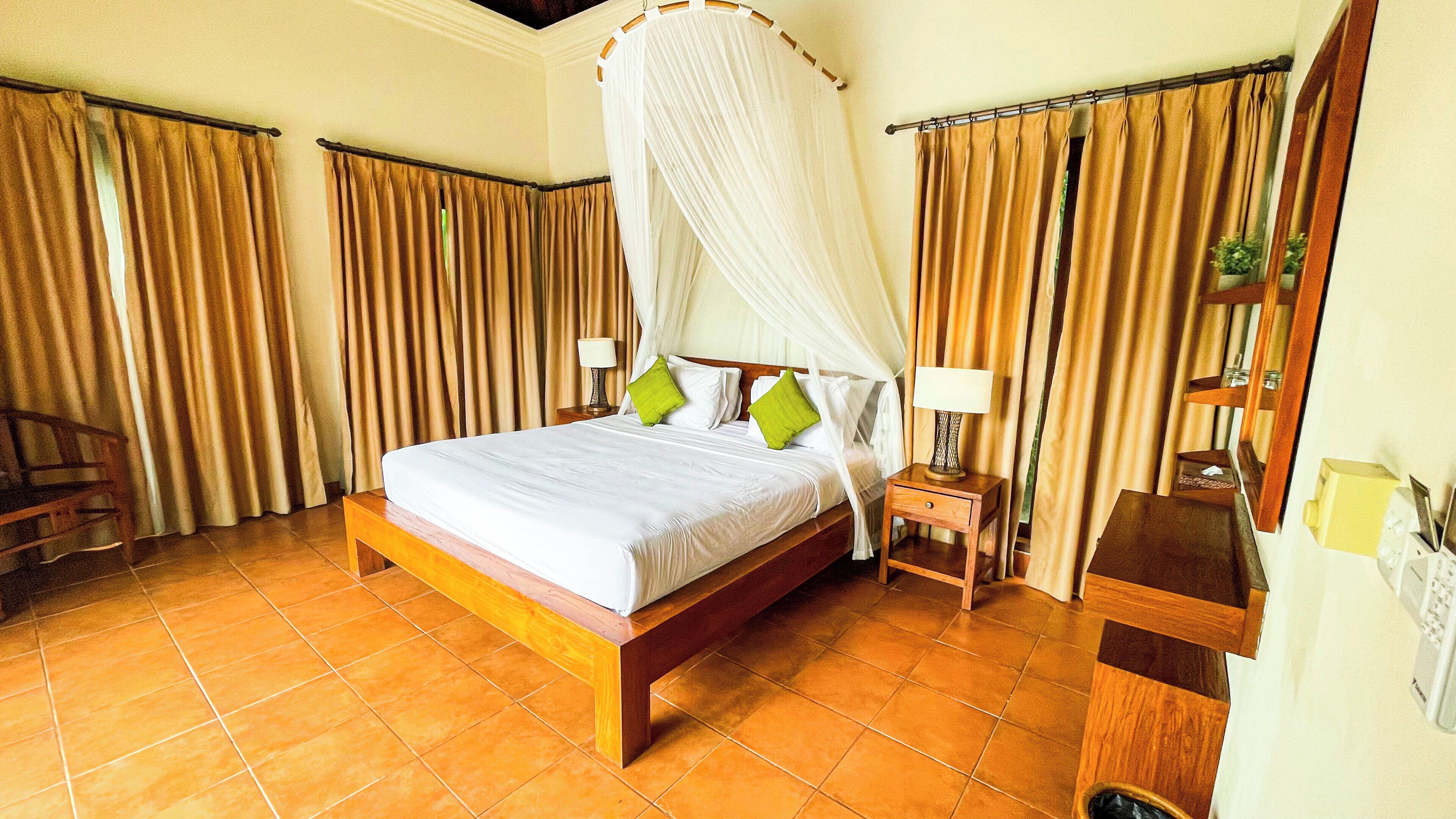 A hotel room with a large bed, curtains, a nightstand, and a bedside table.