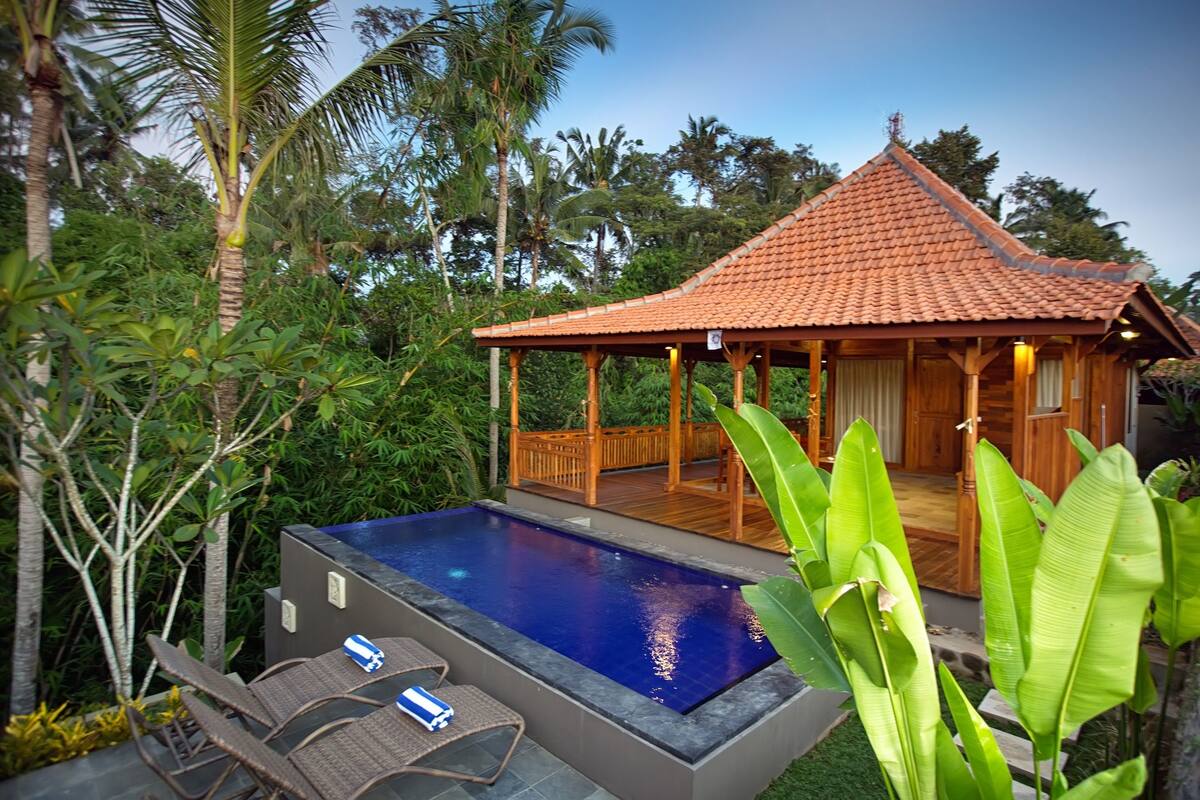 A pool area with a wooden deck, lounge chairs, and a small pavilion.