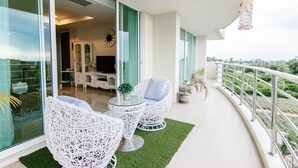 Un balcón con mobiliario de mimbre blanco, una puerta de vidrio que da a una habitación y vistas a la vegetación.