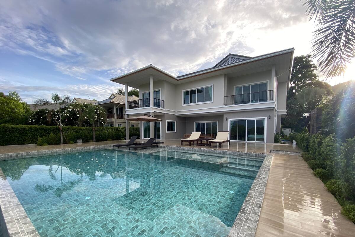 A modern two-story house with a swimming pool, lounge chairs, and a covered patio area.