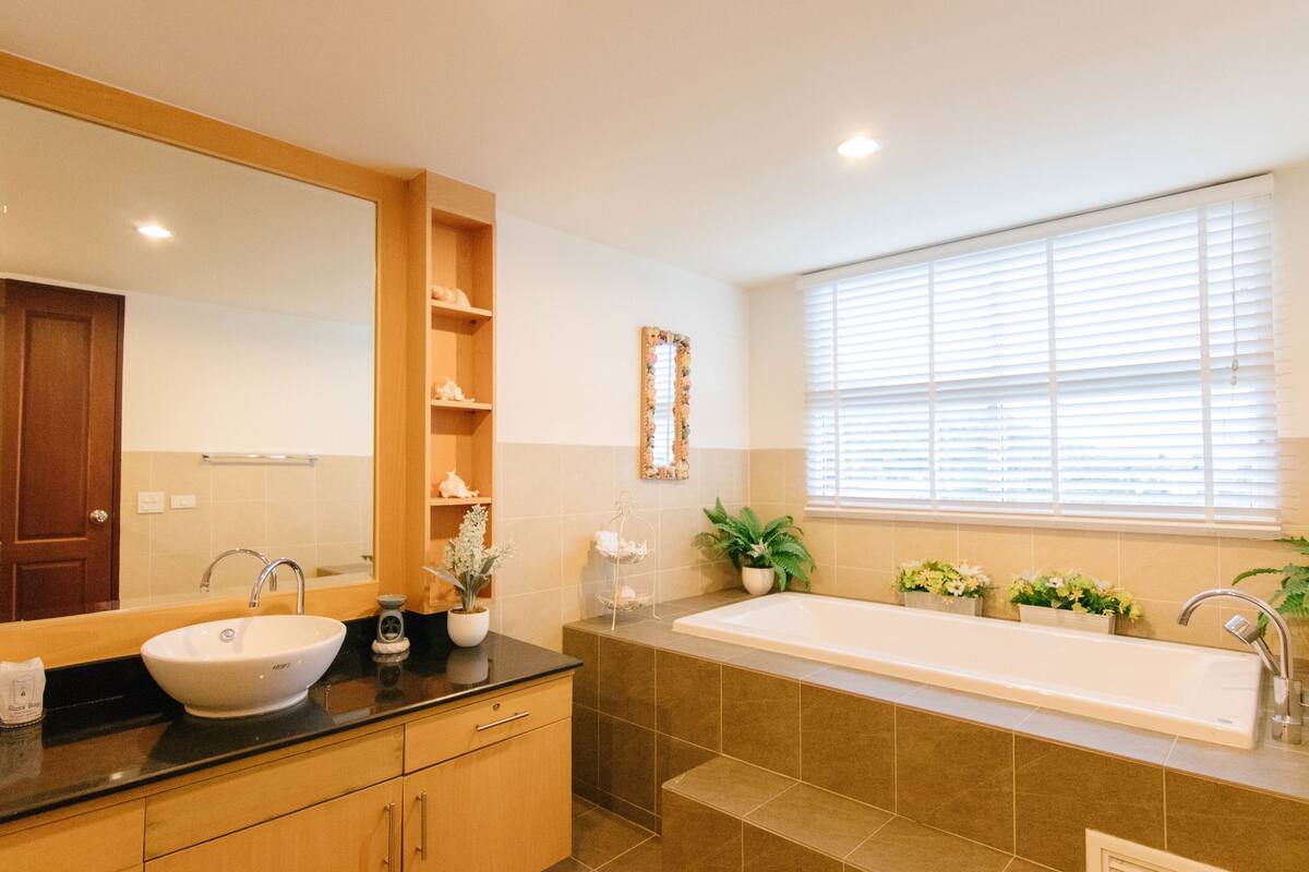 A modern bathroom with a large sink, a bathtub, and a window with blinds.