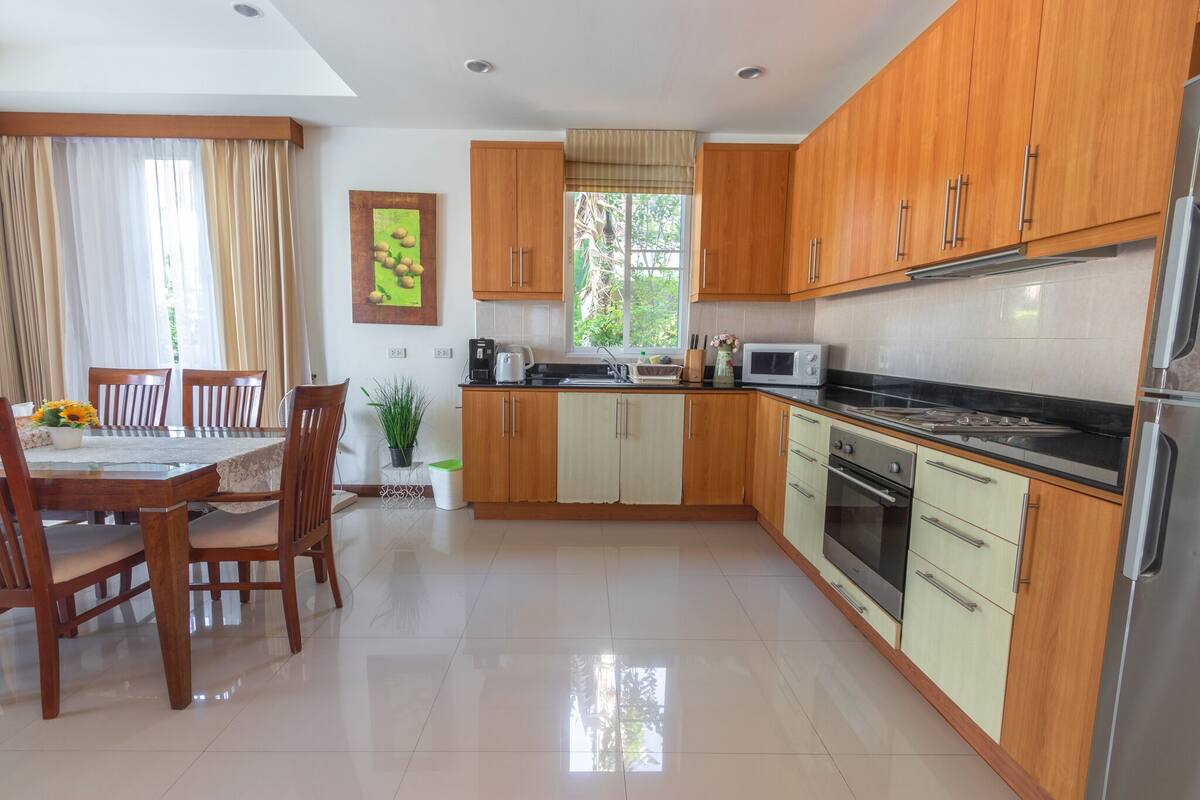 A modern kitchen with wooden cabinets, a stainless steel refrigerator, and a dining area with a table and chairs.