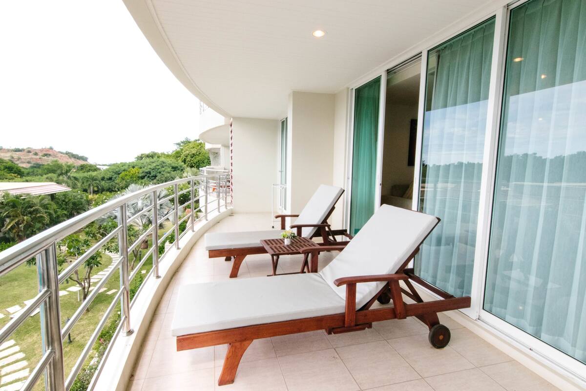 A balcony with two lounge chairs and a small table, overlooking a lush green landscape.