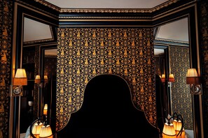 A room with ornate wallpaper, a piano, and wall-mounted lamps.