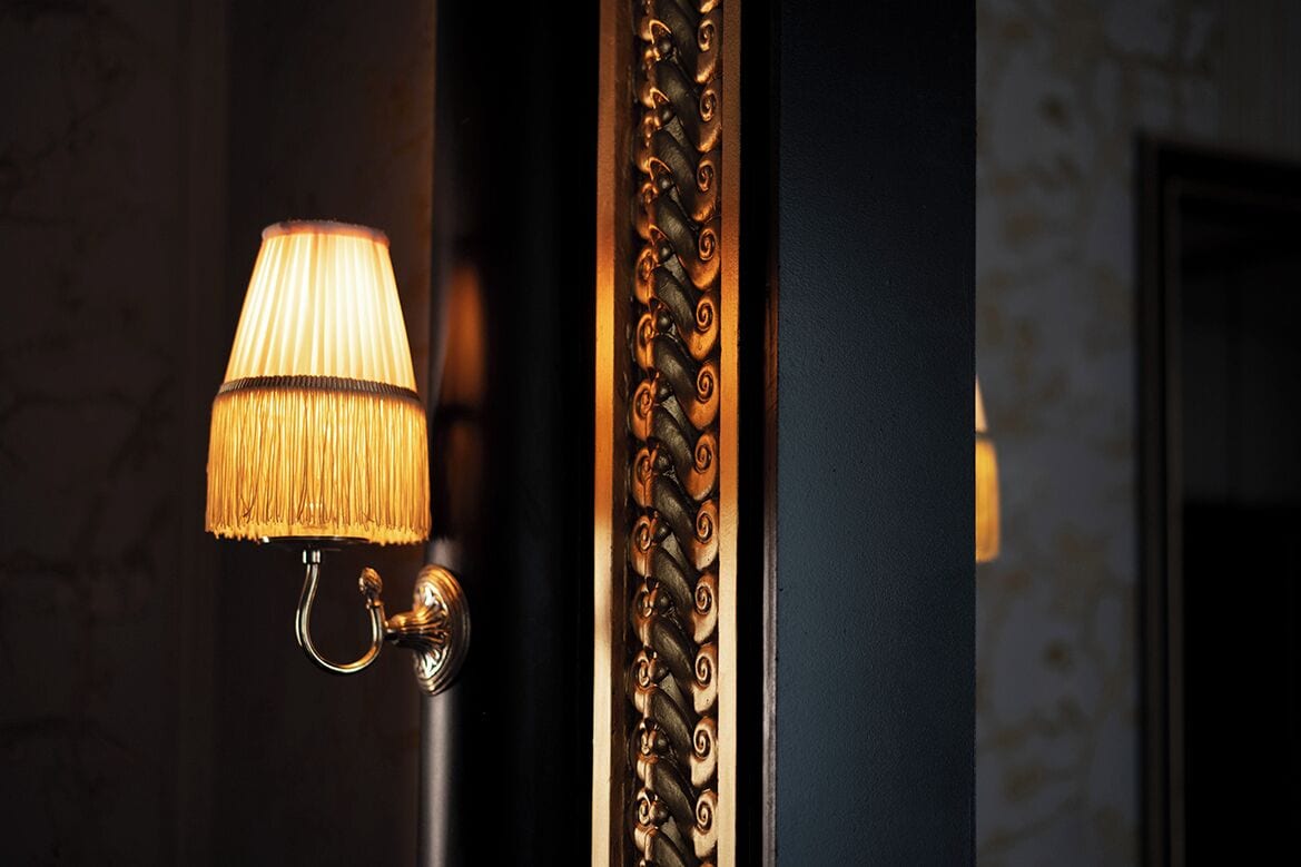Una lámpara de pared con pantalla plisada y un adorno metálico decorativo.