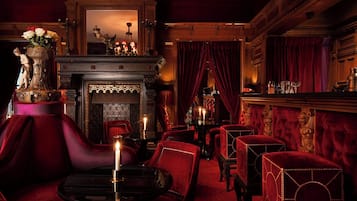 A luxurious room with a fireplace, red velvet chairs, and a bar area.