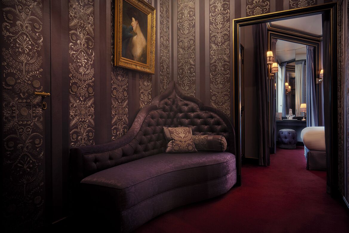 Una habitación lujosa con un sofá de cabecera capitonado, paneles decorativos en la pared y un espejo grande que refleja un espacio bien iluminado.