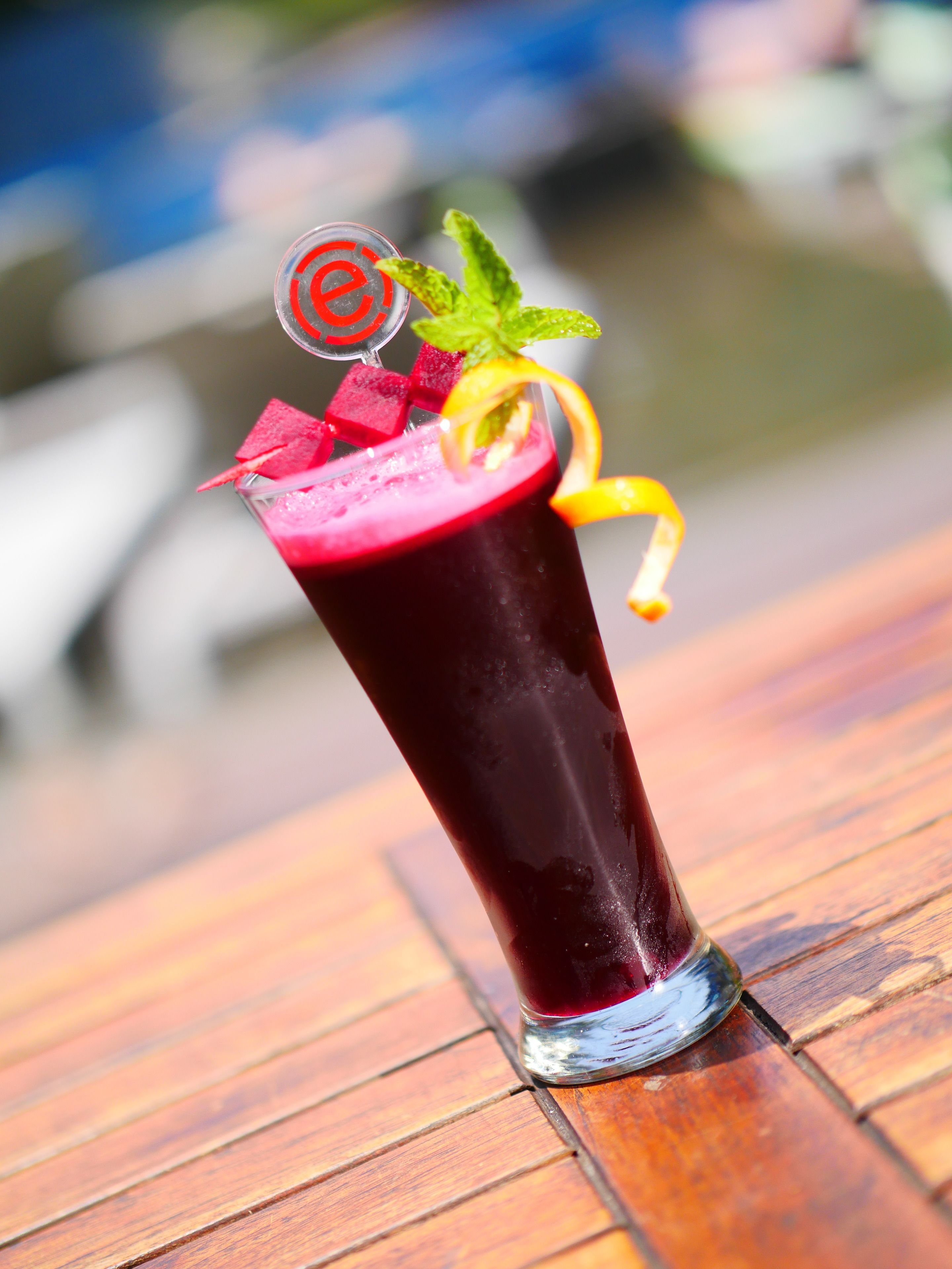 A tall glass with a dark red beverage, garnished with a mint leaf, a slice of lime, and a decorative item.