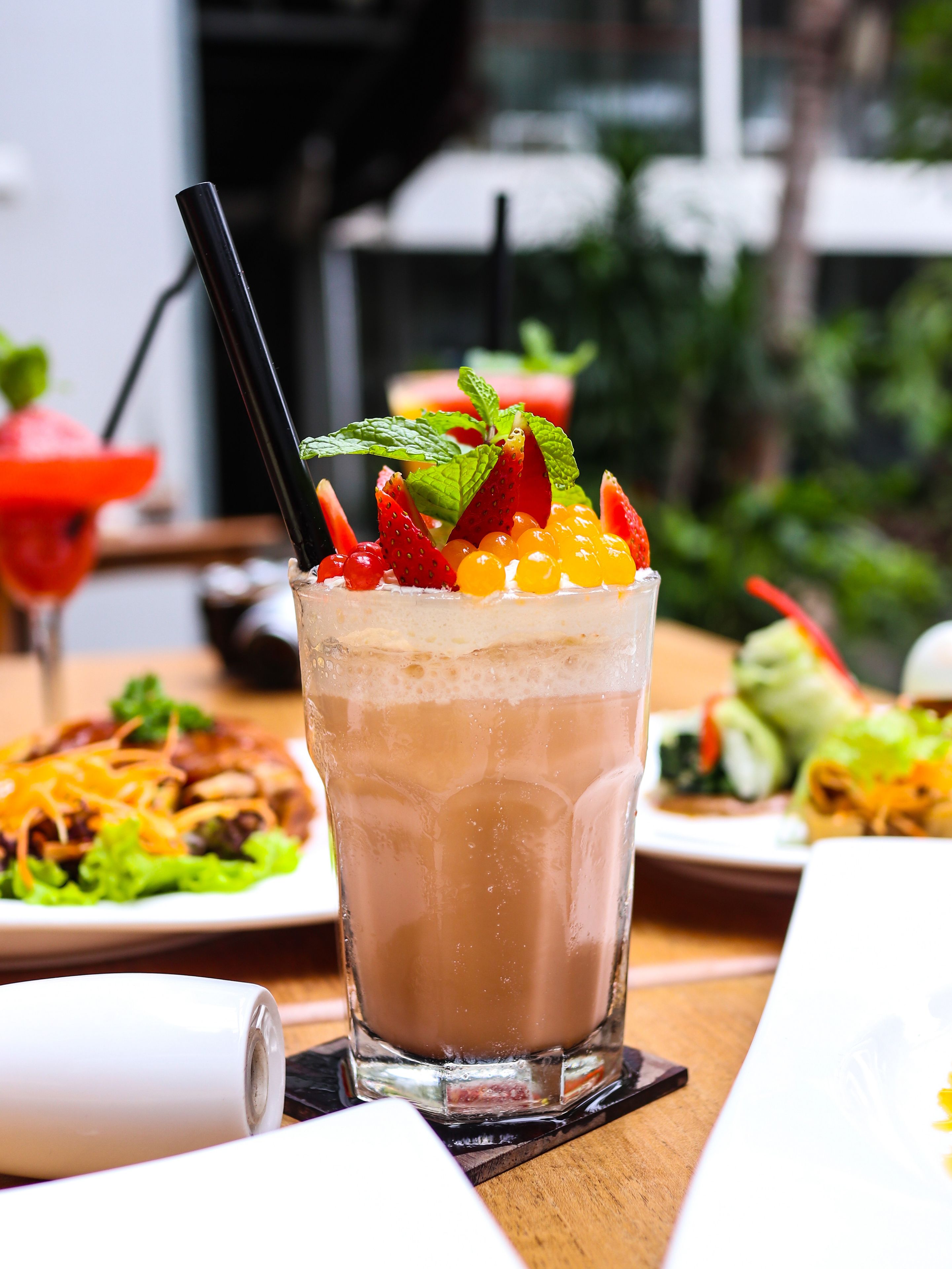 A glass of iced coffee with fruit garnish on a table with various dishes.