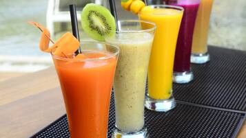 Egy asztalon, színes smoothie-k sorakoznak, a háttérben pedig a medence látható.