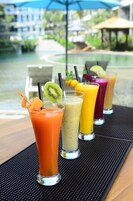 Egy asztalon, színes smoothie-k sorakoznak, a háttérben pedig a medence látható.