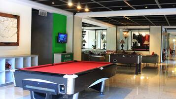 A pool table in a well-lit indoor space with a green accent wall, a television, and a sofa in the background.